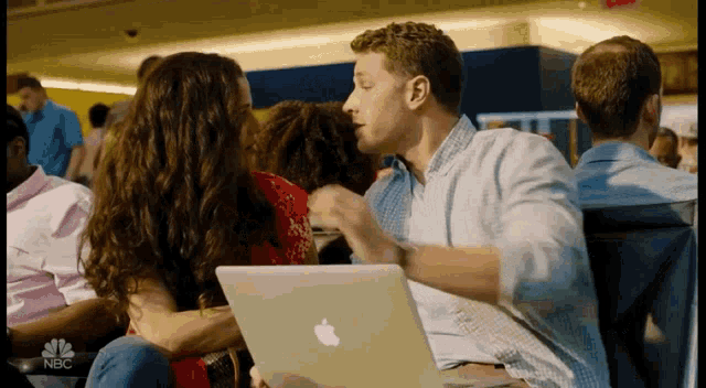 a man and a woman are kissing while sitting in front of an apple laptop