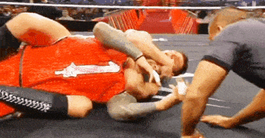 two men are wrestling in a wrestling ring and one of them is wearing a red shirt .