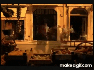 a group of people are standing outside of a store with boxes of fruit on the ground