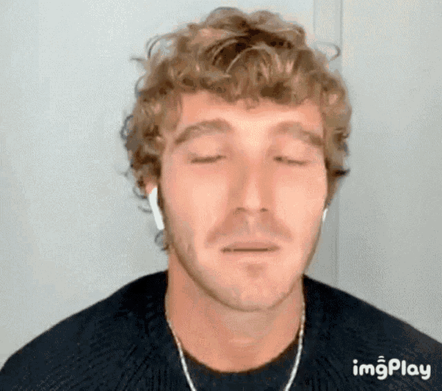 a man with curly hair is wearing headphones and making a funny face with his eyes closed .