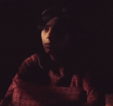 a woman in a red shirt is looking at the camera in the dark