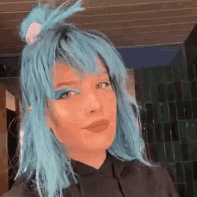a woman with blue hair and blue eyeshadow is wearing a black hoodie and a blue wig .