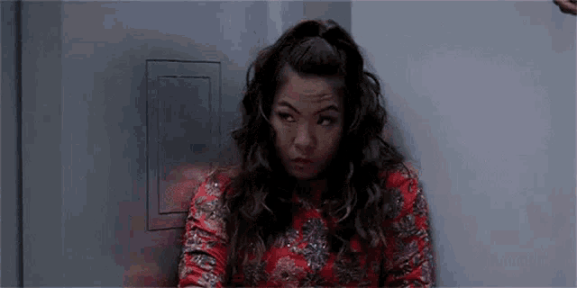 a woman in a red dress is leaning against a wall making a funny face .