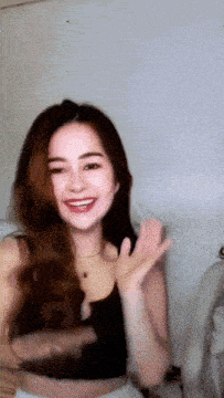 a woman in a black tank top is smiling and waving her hand