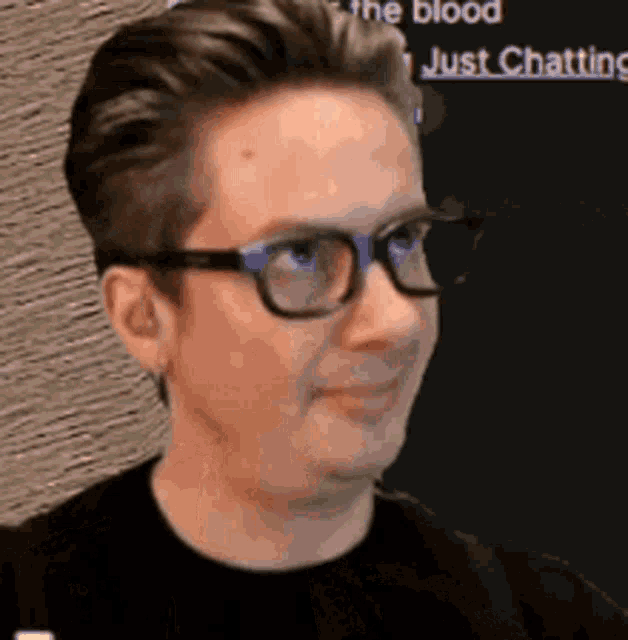 a man wearing glasses and a black shirt is smiling and looking to the side .