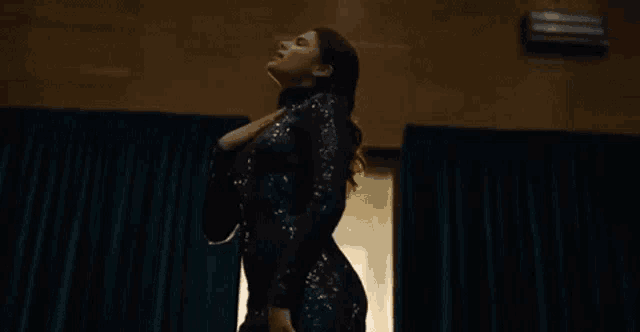 a woman in a black dress is dancing in front of a blue curtain in a dark room .