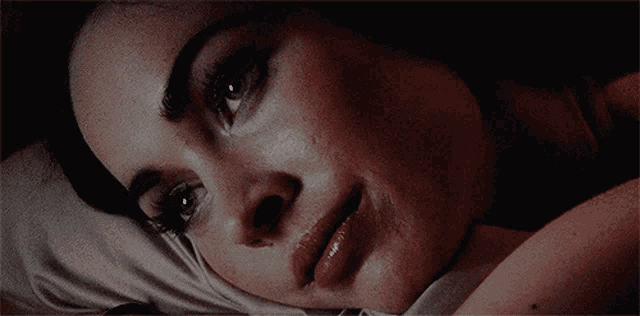 a close up of a woman laying on a bed with her eyes closed
