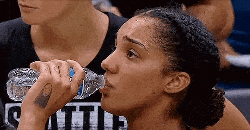 a woman is drinking water from a bottle while sitting in a crowd .