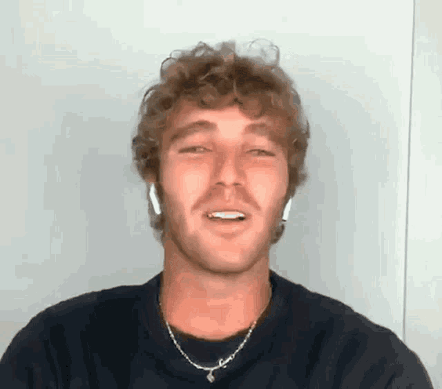 a man with curly hair is wearing a necklace and earbuds .