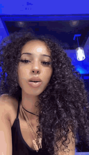 a woman with curly hair is wearing a black tank top and a necklace