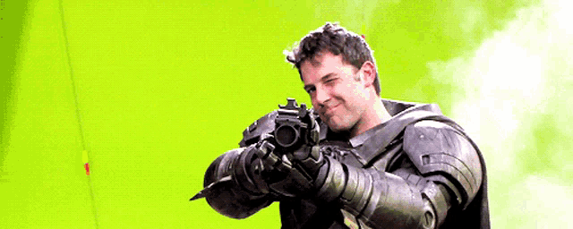 a man in armor is holding a gun in front of a green screen .