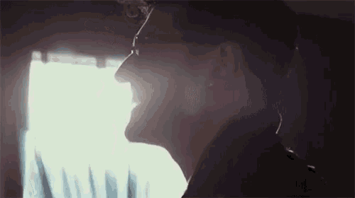 a man wearing glasses is smiling in front of a window in a dark room .