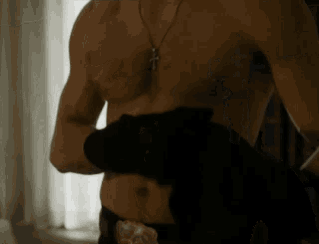 a shirtless man with a cross necklace is holding a black object