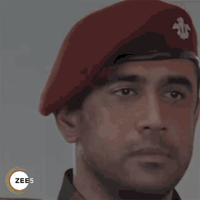 a close up of a man wearing a red beret with a badge on it
