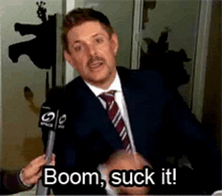 a man in a suit and tie is holding a microphone and says boom , suck it .