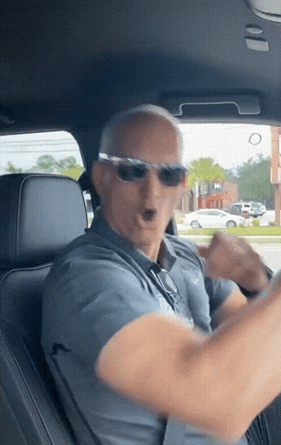 a man wearing sunglasses is driving a car and making a funny face