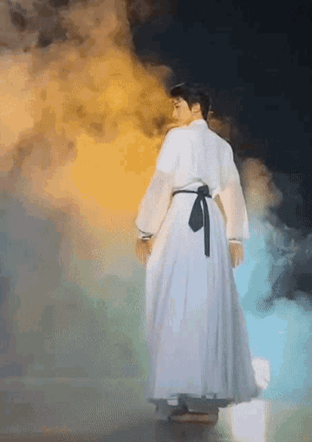 a man in a long white dress is standing in smoke