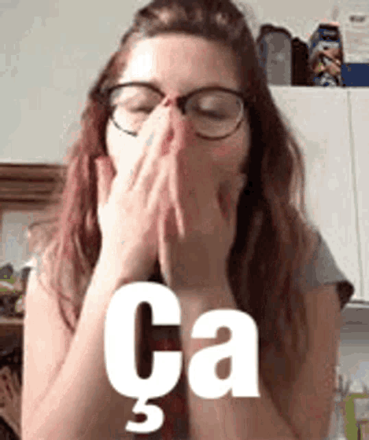 a woman wearing glasses is covering her mouth with her hands and the word ca is on the bottom .