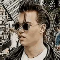 a man wearing sunglasses and a leather jacket is standing in front of a building .