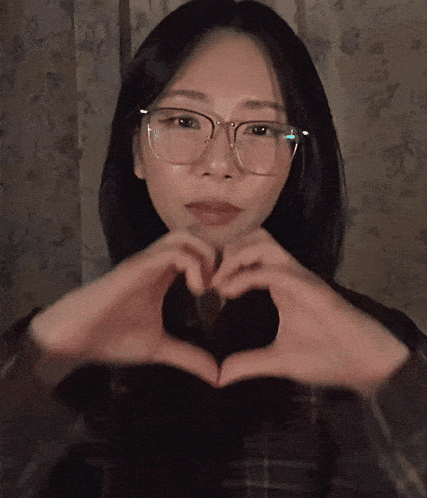 a woman with glasses making a heart shape with her hands