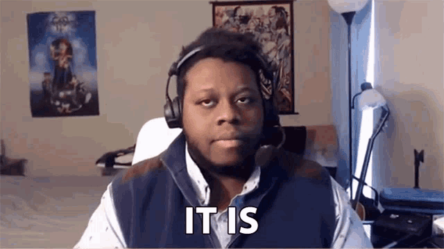 a man wearing headphones and a vest is sitting in front of a computer and says it is .