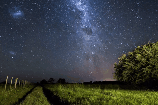 a starry night sky over a grassy field with a fence in the foreground