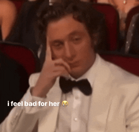 a man in a tuxedo and bow tie is sitting in a theater with his hand on his face .