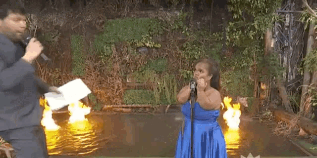 a man in a suit is standing next to a woman in a blue dress holding a microphone in front of a fire .