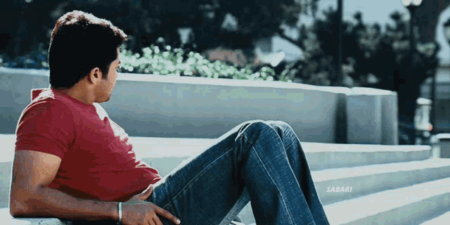 a man in a red shirt sits on a set of stairs with the word sabari on the bottom