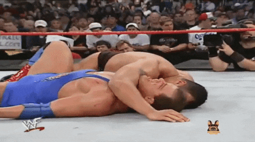two men are wrestling in a wrestling ring and one of them is wearing a blue singlet .