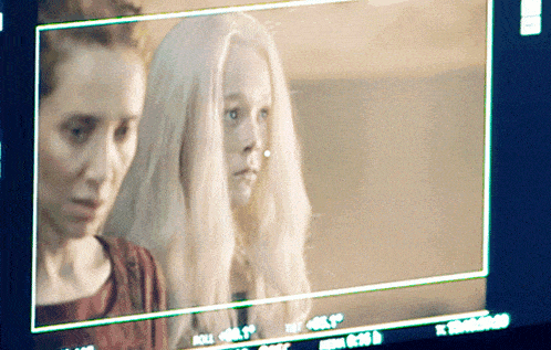 a woman with long white hair stands next to another woman on a monitor
