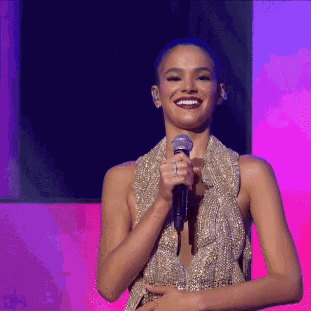 a woman in a gold dress holds a microphone and smiles