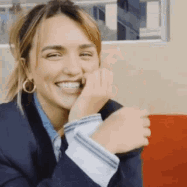 a woman in a suit is smiling and covering her mouth with her hand .