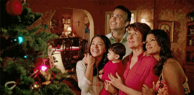 a family is standing around a christmas tree .