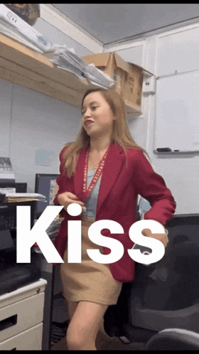 a woman in a red jacket stands in front of a white board with the word kiss on it