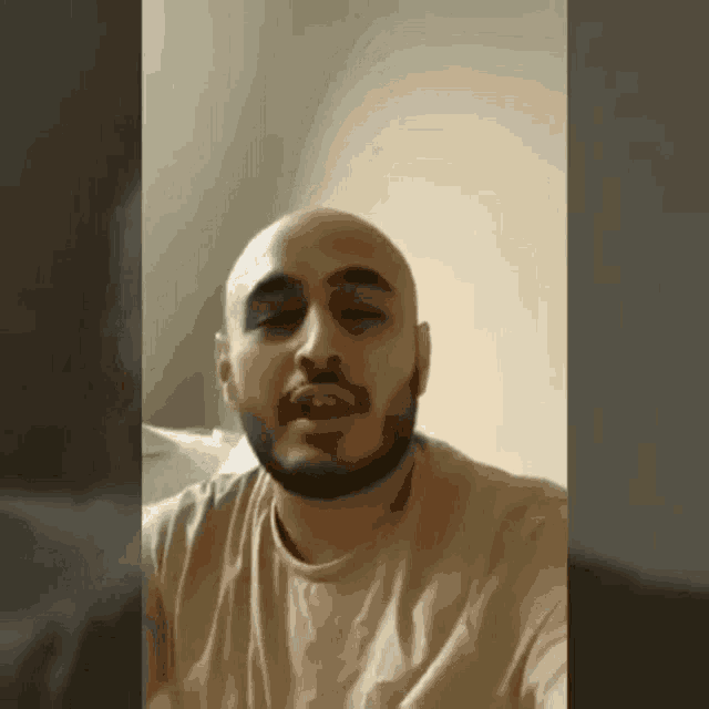 a bald man with a beard is wearing a tan t-shirt