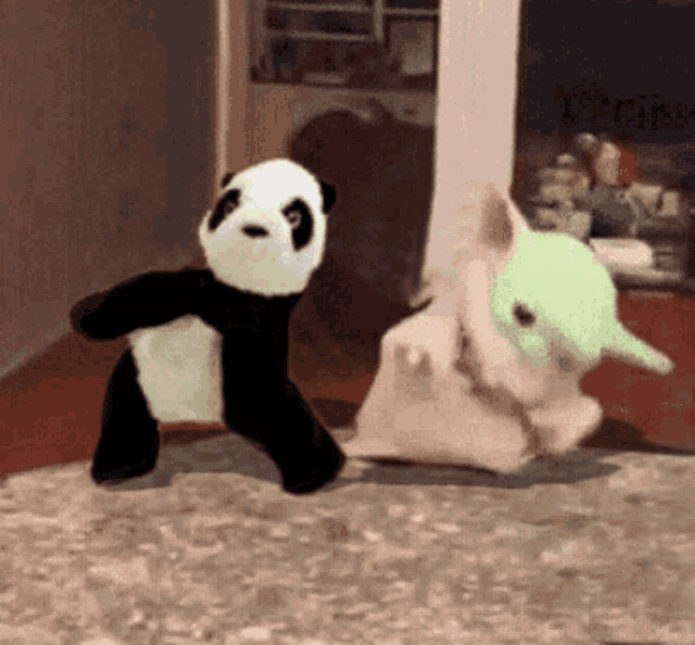 a panda bear and a baby yoda stuffed animal are dancing together on a rug .