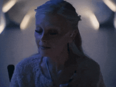 a woman in a white sweater is sitting in a dark room with her eyes closed