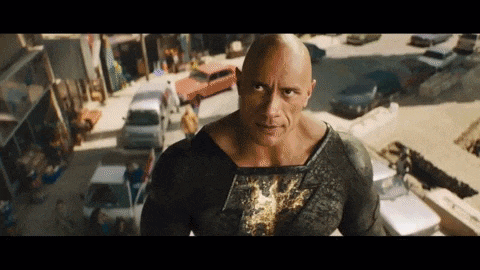 a bald man in a black and gold superhero costume is standing in a busy street .