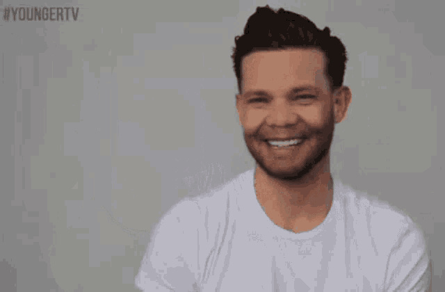 a man in a white t-shirt is smiling in front of a youngertv sign