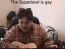 a man in a plaid shirt is sitting at a table playing a guitar and talking .