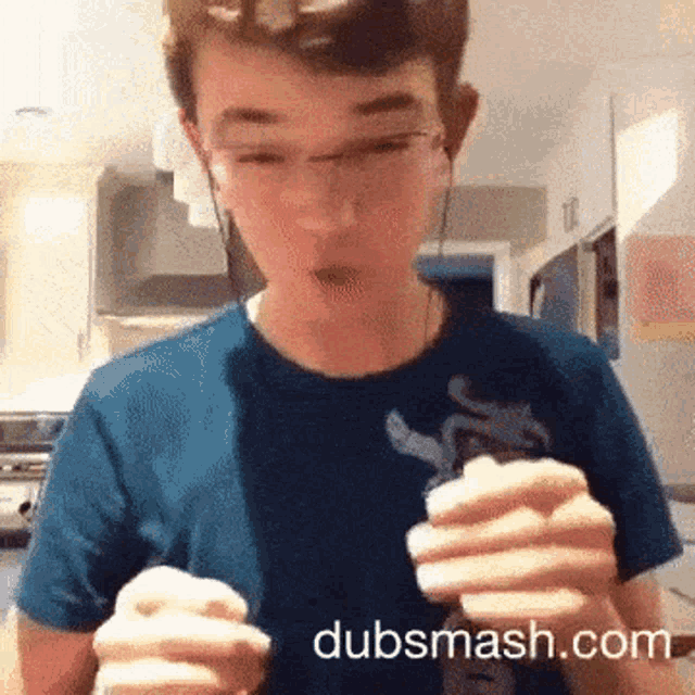 a young man in a blue shirt is holding something in his hands with dubsmash.com written on the bottom right