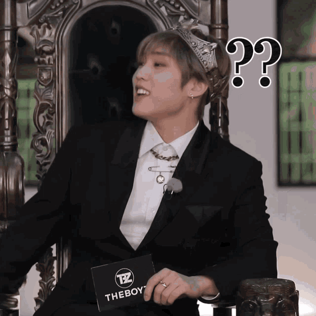 a man wearing a crown is sitting on a throne and holding a card that says theboy