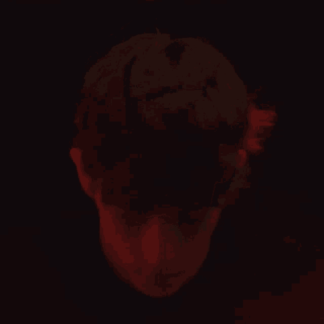 a close up of a man 's face in a dark room with red lights behind him