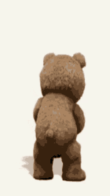 a teddy bear is standing and holding a bottle in its hand .