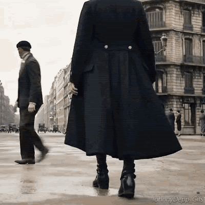 a woman in a long black coat is walking down a street while a man in a suit walks behind her .