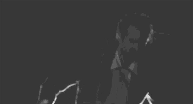 a black and white photo of a man in a suit and tie standing in the dark .