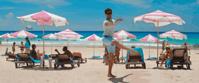 a man stands on one leg on a beach surrounded by pink and white umbrellas