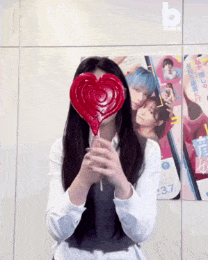 a girl holds a heart shaped lollipop in front of her face