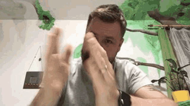 a man is making a peace sign with his hands while sitting in front of a green wall .